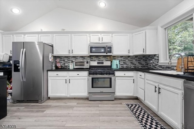 kitchen with dark countertops, a sink, lofted ceiling, stainless steel appliances, and white cabinetry