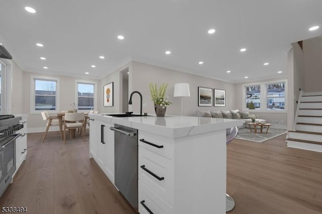 kitchen with white cabinets, a sink, appliances with stainless steel finishes, wood finished floors, and a center island with sink