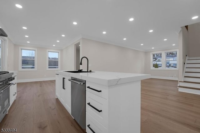 kitchen with a kitchen island with sink, a sink, stainless steel appliances, light wood-type flooring, and baseboards