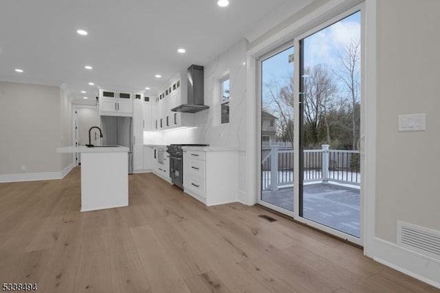 kitchen with wall chimney range hood, light wood-type flooring, a sink, visible vents, and high end stainless steel range oven