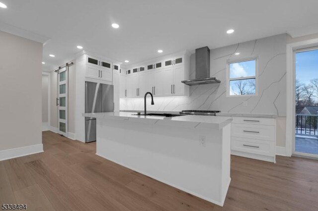 kitchen with a sink, a barn door, freestanding refrigerator, wall chimney exhaust hood, and wood finished floors