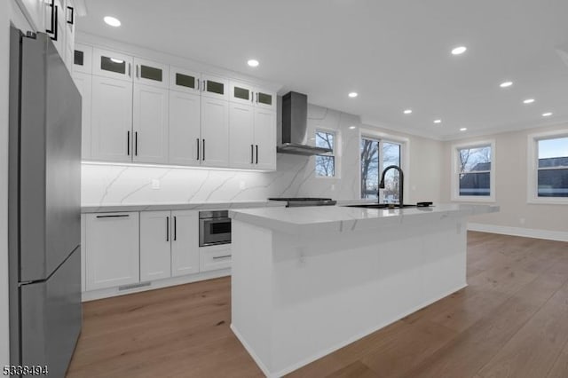 kitchen with light wood-style flooring, wall chimney exhaust hood, oven, and freestanding refrigerator