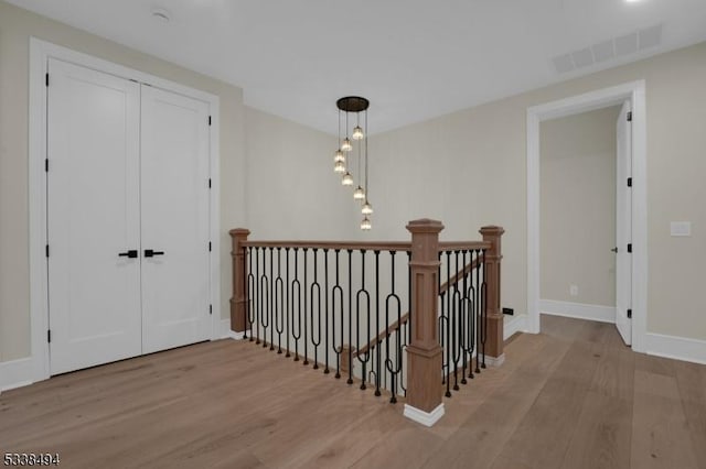 hall with an upstairs landing, wood finished floors, visible vents, and baseboards