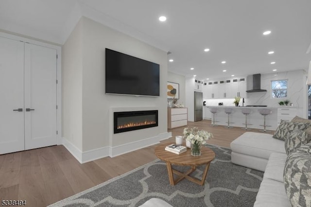 living room featuring a glass covered fireplace, light wood-type flooring, recessed lighting, and baseboards