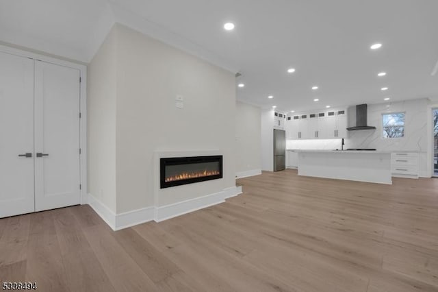 unfurnished living room with light wood finished floors, recessed lighting, baseboards, and a glass covered fireplace