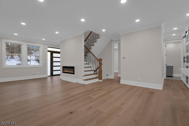 unfurnished living room featuring recessed lighting, light wood-style floors, a glass covered fireplace, stairs, and baseboards