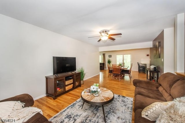 living room featuring baseboards, ceiling fan, and light wood finished floors