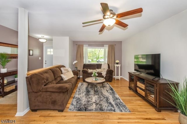 living area with baseboards, a ceiling fan, and light wood finished floors