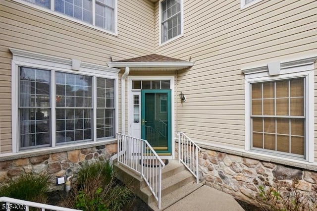 doorway to property featuring a shingled roof and stone siding