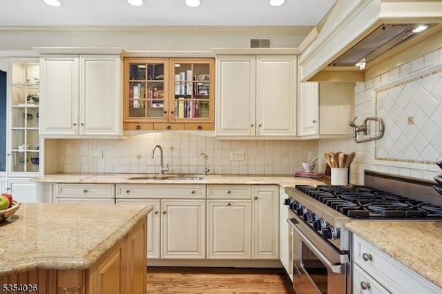 kitchen with visible vents, high end stove, a sink, custom exhaust hood, and glass insert cabinets