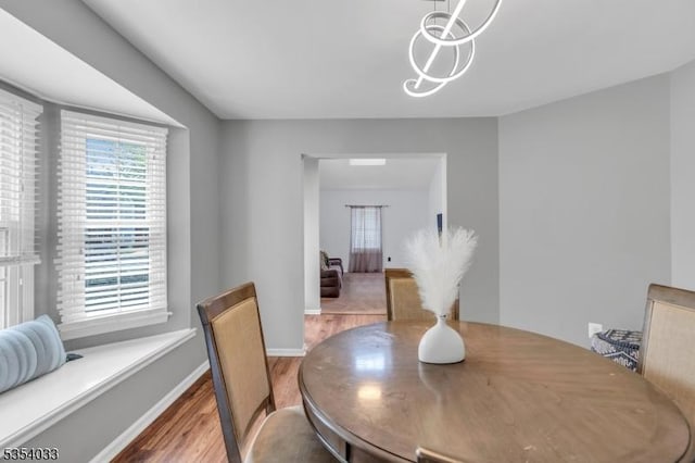 dining space with baseboards, an inviting chandelier, plenty of natural light, and wood finished floors