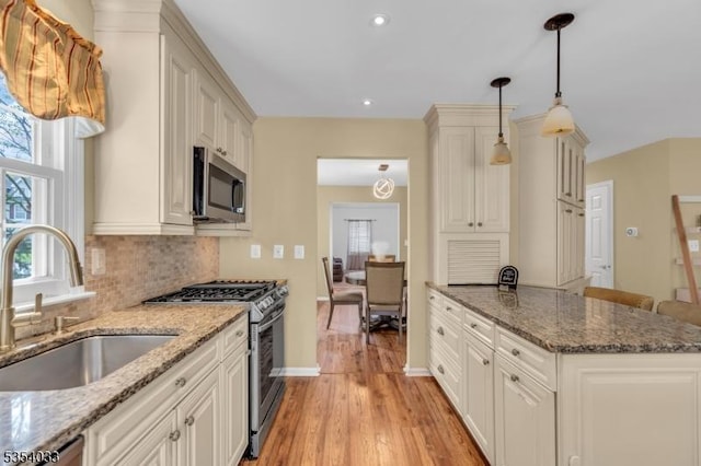 kitchen with backsplash, light wood-type flooring, a sink, stone counters, and stainless steel appliances
