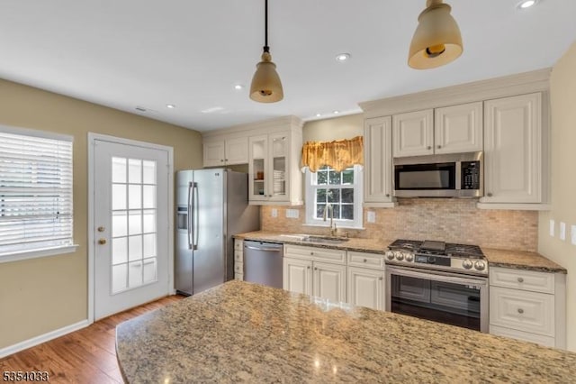 kitchen featuring light stone counters, a sink, light wood-style floors, stainless steel appliances, and tasteful backsplash
