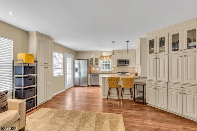 kitchen with a breakfast bar area, backsplash, appliances with stainless steel finishes, light wood-type flooring, and cream cabinetry