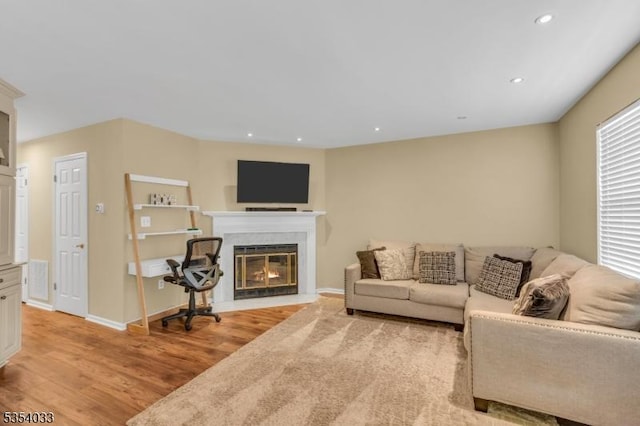 living room featuring recessed lighting, a fireplace with flush hearth, light wood-style flooring, and baseboards