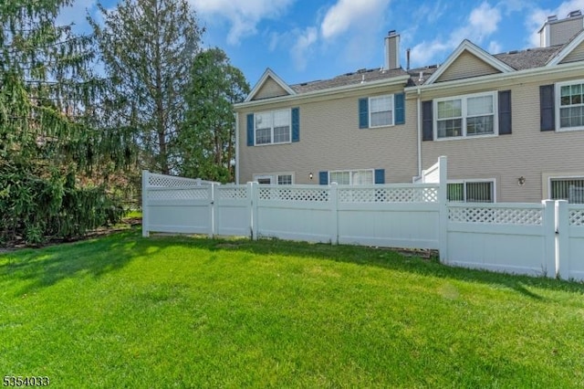 rear view of house featuring a lawn, fence, and a chimney