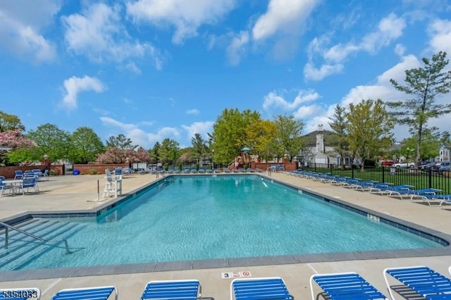 community pool with a patio area, fence, and playground community