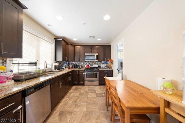 kitchen featuring dark brown cabinetry, a sink, stainless steel appliances, decorative backsplash, and visible vents