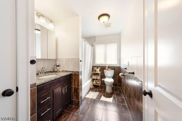 full bath featuring tile walls, tile patterned flooring, a wainscoted wall, vanity, and toilet