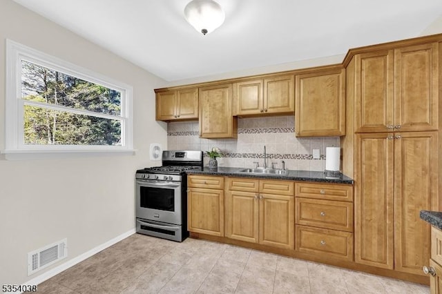 kitchen featuring visible vents, decorative backsplash, stainless steel gas stove, baseboards, and a sink
