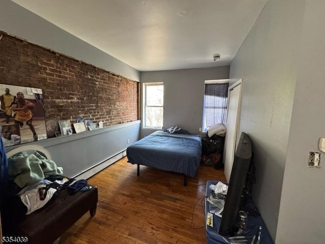 bedroom with wood finished floors, baseboard heating, and brick wall