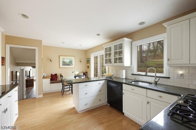 kitchen featuring dark countertops, a sink, a peninsula, light wood-type flooring, and black appliances