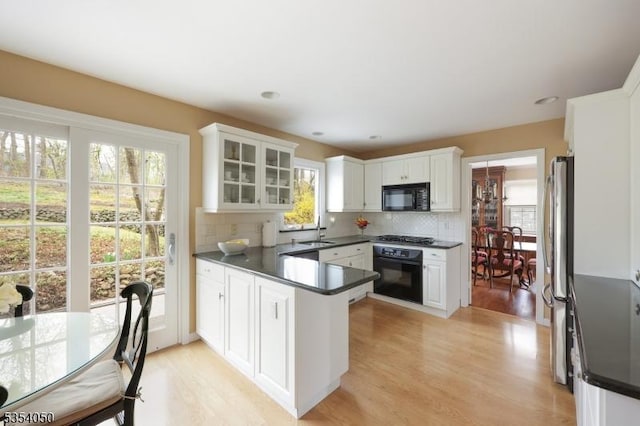 kitchen with a peninsula, dark countertops, light wood-type flooring, a sink, and black appliances