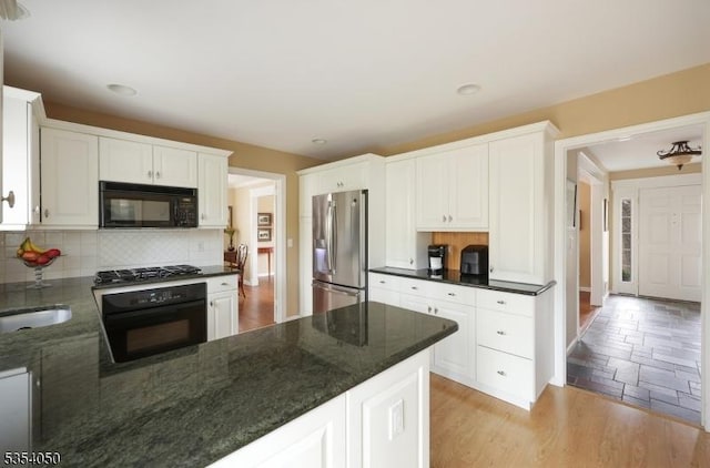 kitchen with dark stone counters, backsplash, black appliances, and white cabinetry