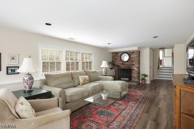 living area featuring dark wood-style flooring, visible vents, stairway, and a fireplace