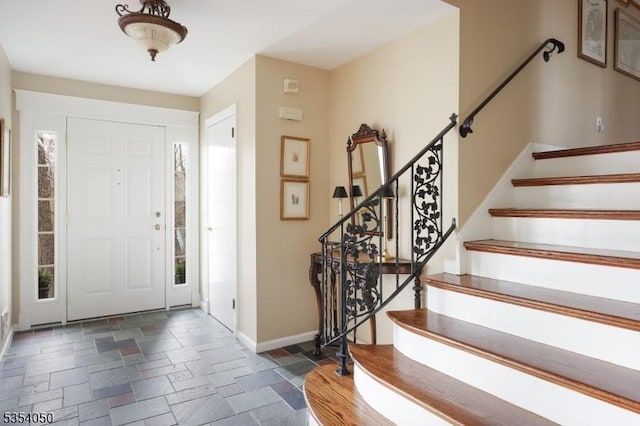 foyer entrance with baseboards, stone tile floors, and stairs