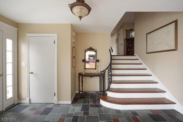 foyer with a healthy amount of sunlight, baseboards, stairway, and stone finish flooring