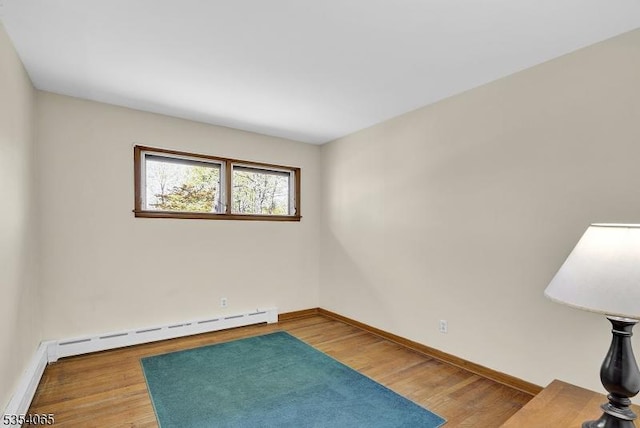 spare room with baseboards, a baseboard heating unit, and wood finished floors