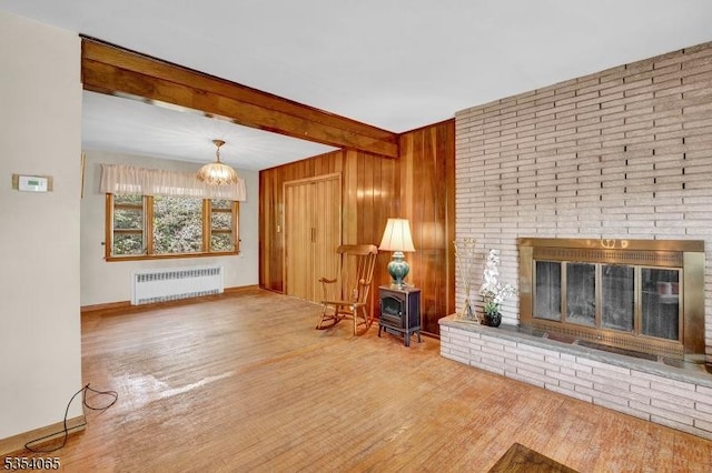 living room with a brick fireplace, a chandelier, radiator, wood finished floors, and beamed ceiling