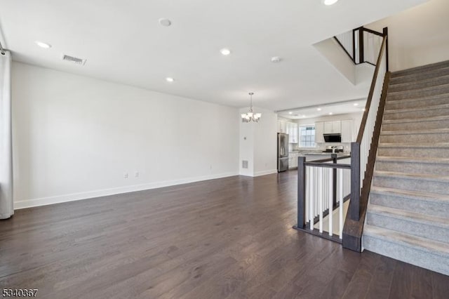 unfurnished living room featuring an inviting chandelier, recessed lighting, baseboards, visible vents, and dark wood-style floors