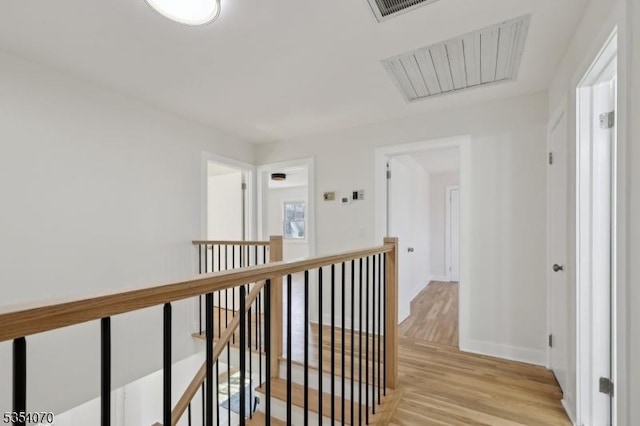 corridor featuring light wood-type flooring, baseboards, visible vents, and an upstairs landing