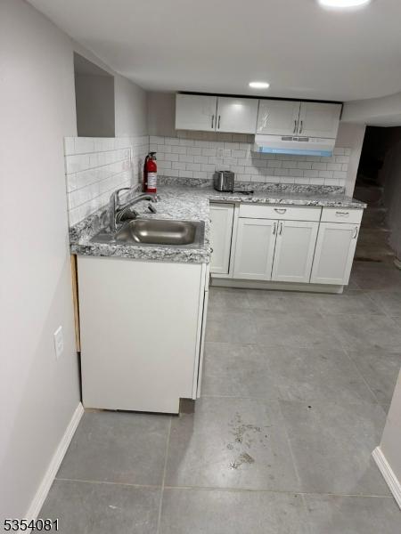 914 S St, Elizabeth City, NJ 07202 - kitchen with a sink, white cabinetry, baseboards, tasteful backsplash, and under cabinet range hood
