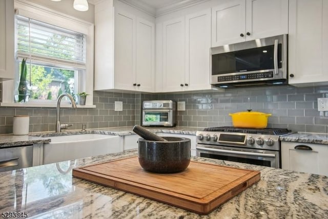 kitchen featuring white cabinets, light stone counters, a sink, appliances with stainless steel finishes, and backsplash