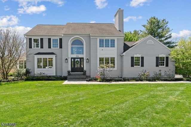 colonial inspired home with a chimney and a front lawn