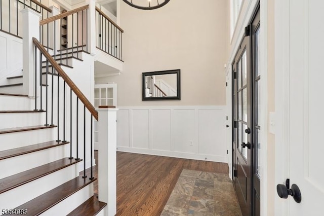 entryway with stairs, dark wood-style flooring, a towering ceiling, a decorative wall, and wainscoting