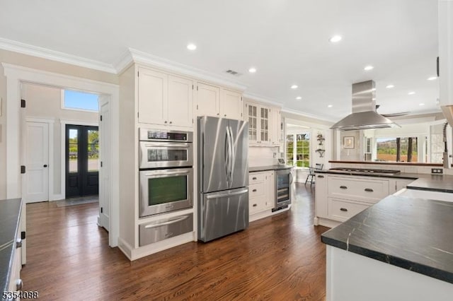 kitchen with island range hood, appliances with stainless steel finishes, dark countertops, beverage cooler, and a warming drawer