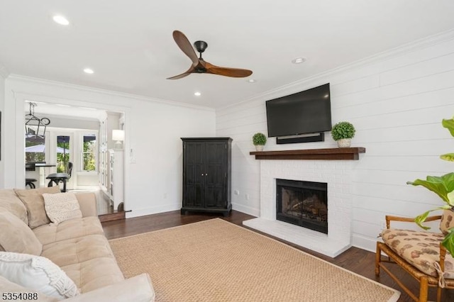 living area with a ceiling fan, a brick fireplace, wood finished floors, and ornamental molding