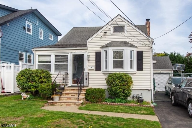 view of front of house featuring a front lawn, fence, a chimney, a shingled roof, and entry steps
