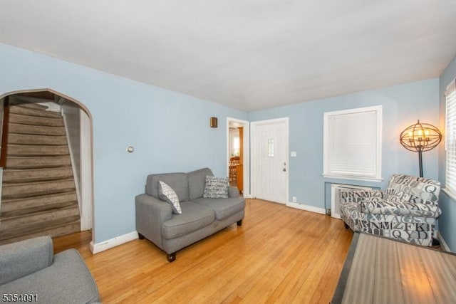 living area featuring light wood-type flooring, arched walkways, baseboards, and stairway