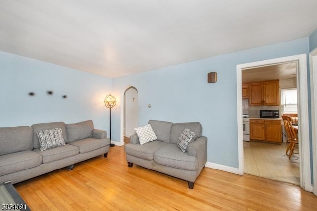 living room with arched walkways, baseboards, and light wood finished floors