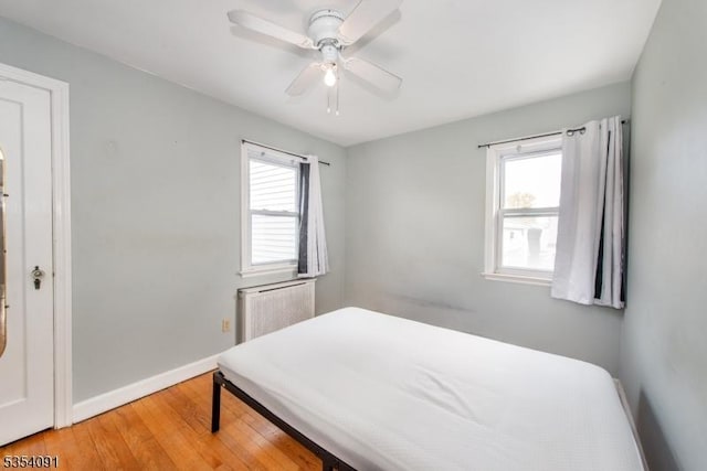bedroom featuring baseboards, light wood-style flooring, radiator, and ceiling fan