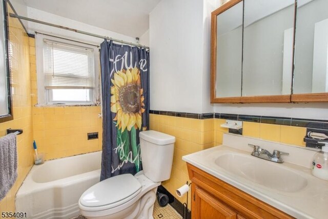 bathroom featuring tile walls, shower / bath combo, wainscoting, vanity, and toilet