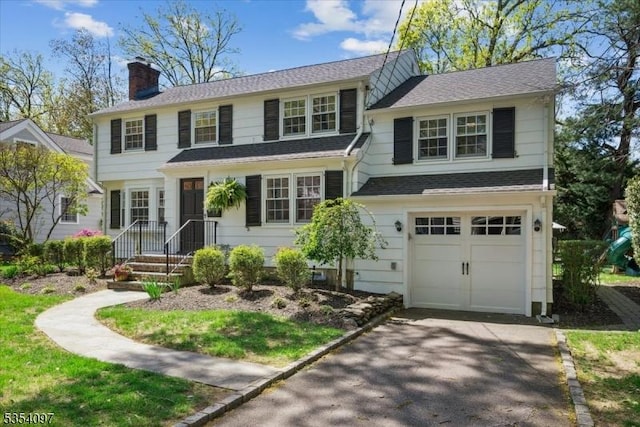 view of front of property featuring an attached garage, a chimney, a shingled roof, and aphalt driveway