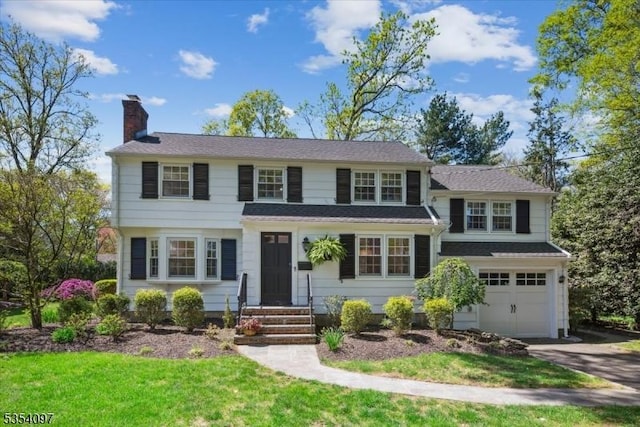 view of front of property with an attached garage, driveway, a chimney, and a front lawn