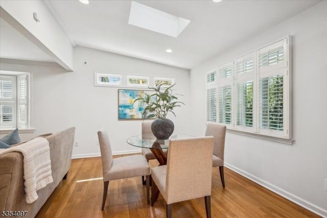 dining room with a healthy amount of sunlight, baseboards, lofted ceiling with skylight, and wood finished floors