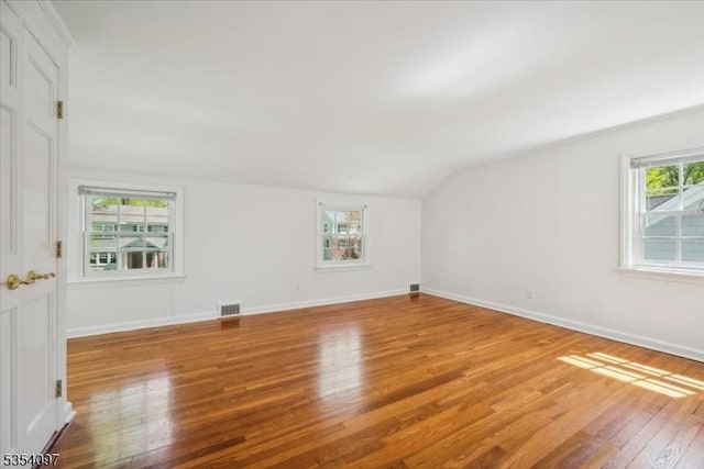 additional living space with baseboards, vaulted ceiling, wood finished floors, and visible vents